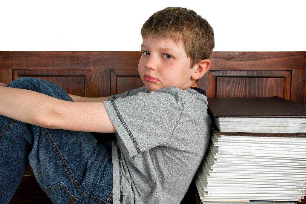 Niño con gesto aburrido apoyado en una pila de libros