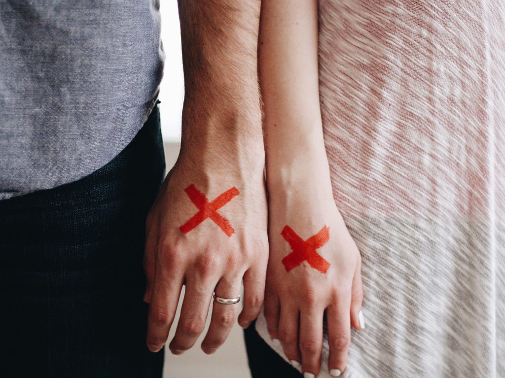 Dos personas con los brazos y manos juntos y una X roja en el dorso de la mano