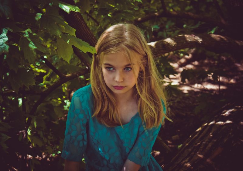 Niña rubia con vestido azul, encaramada en árbol