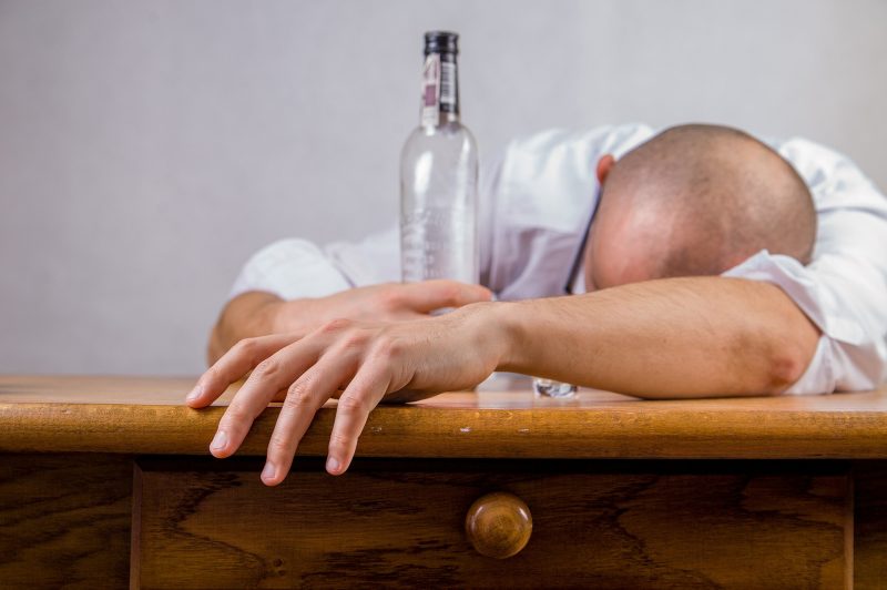 Chico dormido sobre una mesa, agarrando una botella vacía