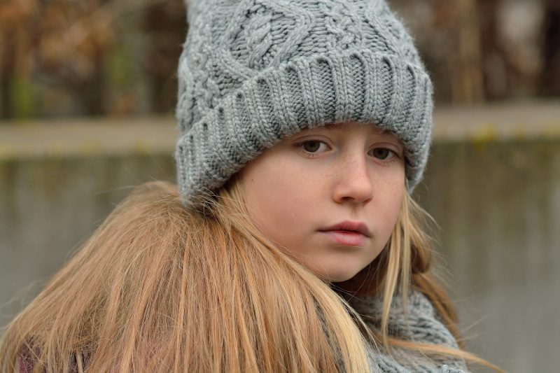 Niña rubia triste con gorro gris de lana