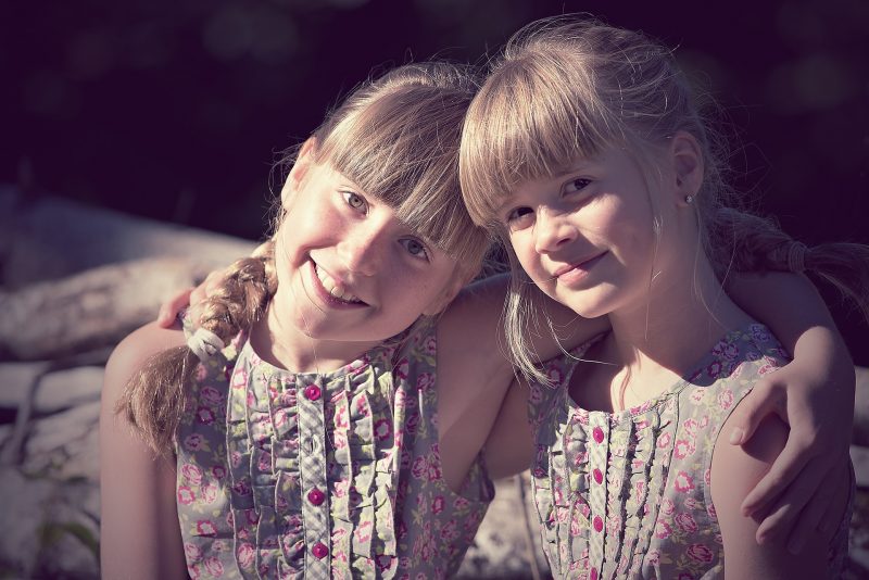 Dos niñas rubias con flequillo y vestidos verdes de flores, agarradas por los hombros