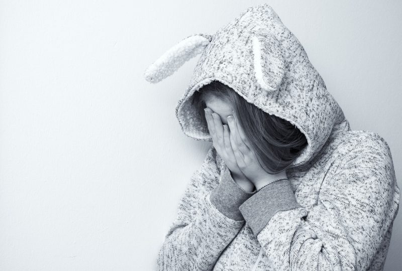 Niño con sudadera con orejas de conejo se tapa la cara con las manos