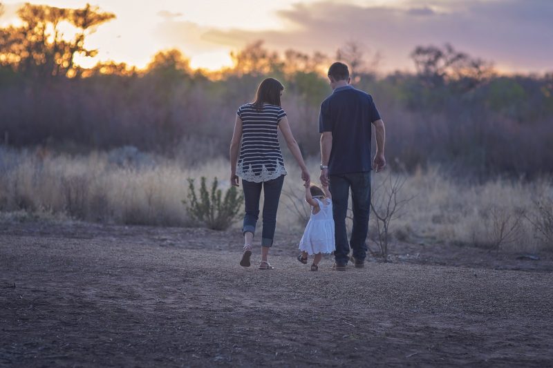 Pareja sostiene de la mano a niña pequeña durante un paseo por el campo