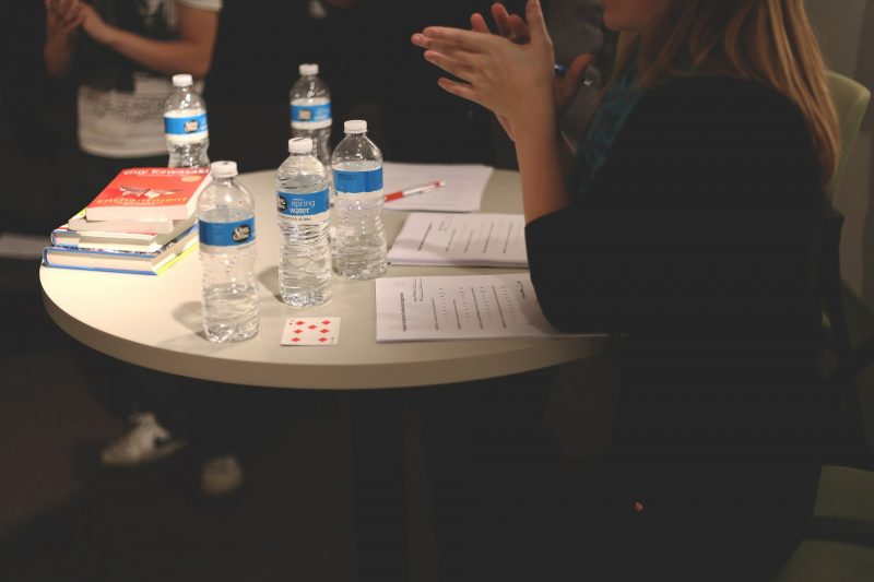 Mujer sentada en una mesa redonda con papeles, libros y botellas de agua