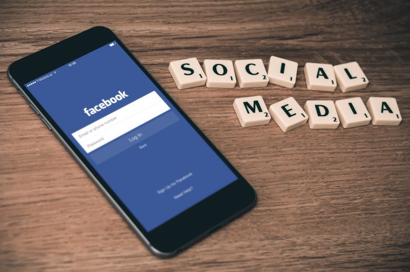 Teléfono mostrando la aplicación Facebook, y las palabras Social Media escritas con letras de Scrabble