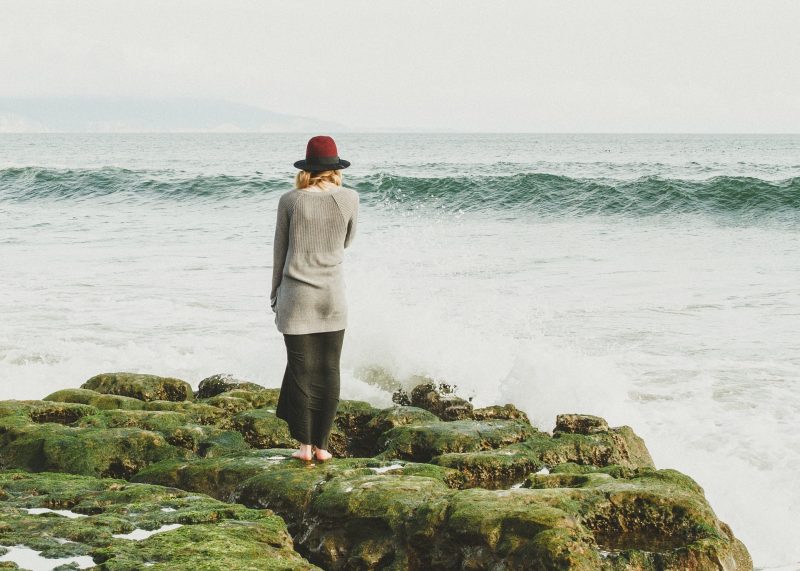 Mujer sobre rocas, mirando al mar