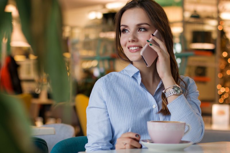 Una chica joven habla por teléfono sentada en una cafetería, con una taza de café delante