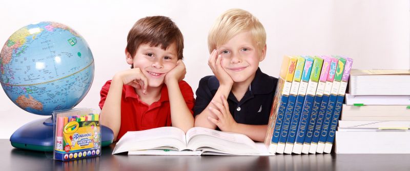 Dos niños con material escolar: enciclopedias, libros de estudio, globo terráqueo y rotuladores