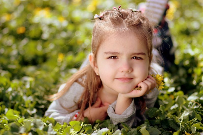 Niña tumbada sobre la hierba, con un ramillete de flores