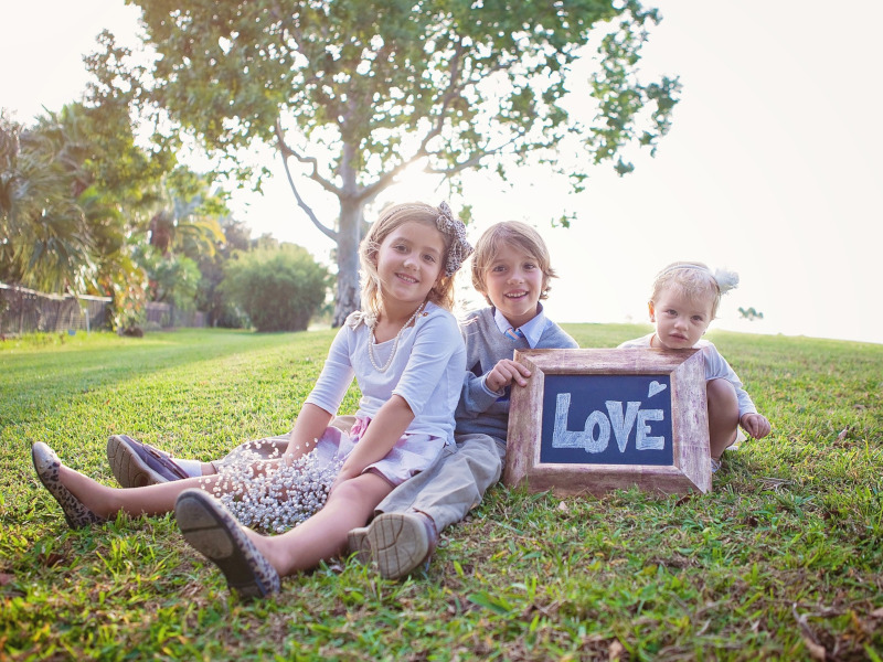 Tres niños sentados en la hierba sujetando un cartel con la palabra LOVE.