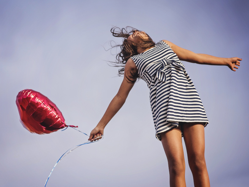 Chica joven saltando con globo en forma de corazón