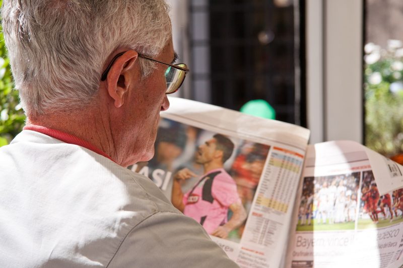 Una persona mayor leyendo un periódico de fútbol.