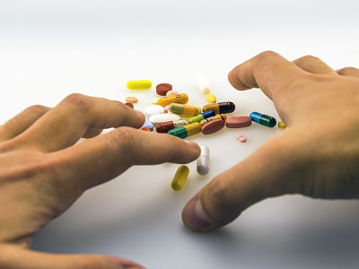 Una mano se dispone a coger medicamentos: pastillas, píldoras, etc... de diferentes colores.