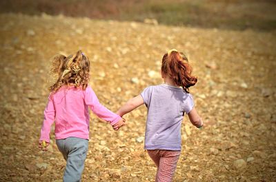 Dos niñas cogidas de la mano y corriendo por un terreno pedregoso.