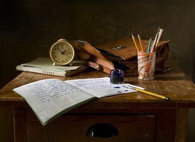 Aparece un pupitre con material escolar: un cuaderno, tintero, varias plumas, libros de texto, una cartera y un reloj.